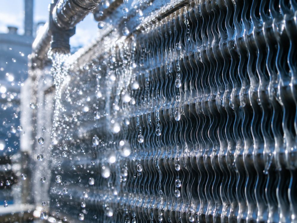 Close-up de aletas de serpentín de condensador evaporativo con gotas de agua a contraluz